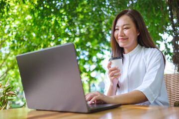 Portrait image of a woman drink coffee while working on laptop computer in the outdoors