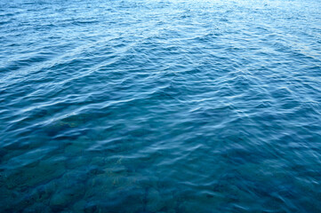 Blue water surface viewed from above in outdoor sea, sun reflection, dimply.
