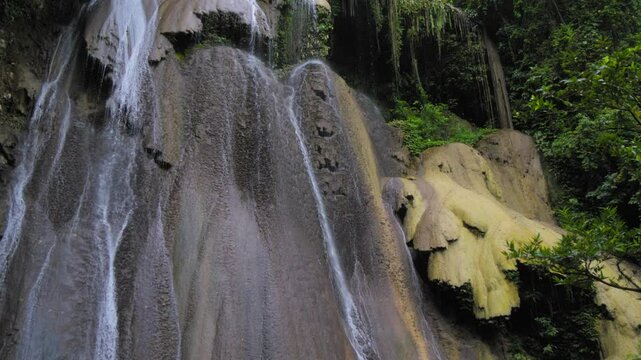 A stunning War Inkabom Waterfall on Batanta Island in Raja Ampat, Indonesia, cascades down a rocky cliff into a serene pool below, surrounded by lush greenery. Tilt-down shot in slow motion.