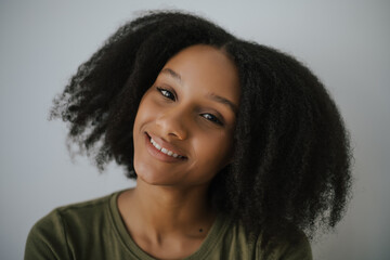 Smiling young African American woman with natural curly hair against light background. 