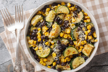Vegetarian salad of roasted zucchini, black beans, corn, garlic and parmesan close-up in a bowl on the table. Horizontal top view from above