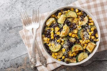 Roasted Zucchini salad with black beans, corn, garlic and cheese close-up in a bowl on the table. Horizontal top view from above
