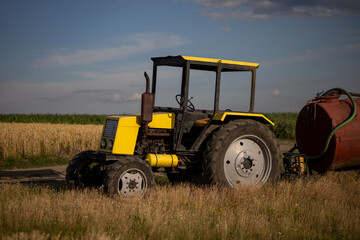 Old yellow tractor in the field with a barrel