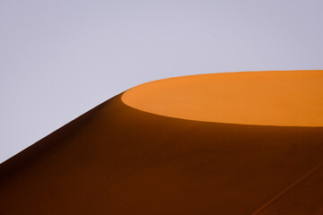 A sunlit sand dune stands out against a clear sky, capturing the minimalist beauty and striking contrasts of the Namibian desert landscape.