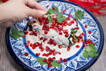 Mexican cooking Chiles en Nogada, traditional mexican plate for mexican independence day with Poblano chili stuffed with beef and pork, mix with pomegranate fruit, nogada, vegetables in wood table  