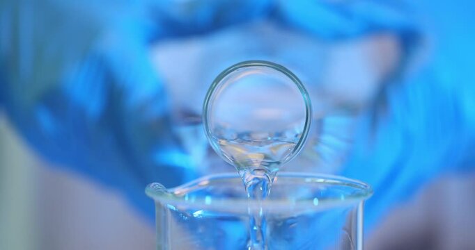 Laboratory worker hands pour water into transparent beaker