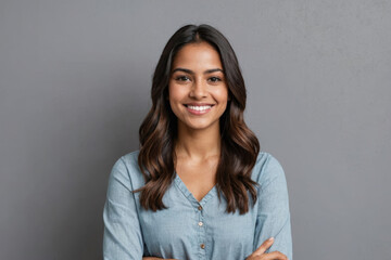 Fototapeta premium Portrait of a young latin woman with pleasant smile and crossed arms isolated on grey wall with copy space. Beautiful girl with folded arms looking at camera against grey wall. Cheerful hispanic woman