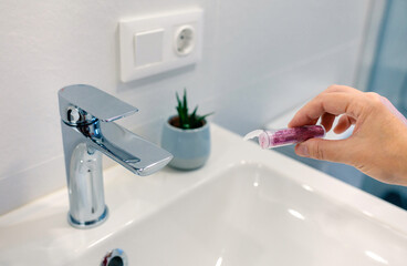 Close up of female hand pouring purple glitter bottle into washbasin at bathroom and polluting clean water. Dangers of microplastics composition to humans and environment concept.