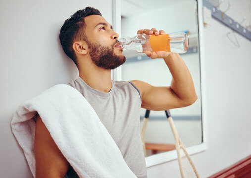 Man, relax and drinking with bottle water for hydration, natural sustainability or break at gym locker room. Young male person in recovery or thirst with mineral beverage on bench at health club - Powered by Adobe