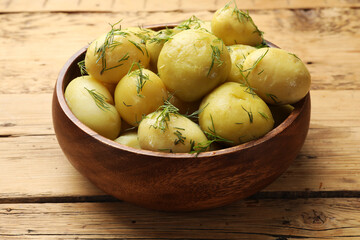Tasty young boiled potatoes with dill in bowl on wooden table, closeup