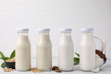 Different types of vegan milk in bottles and ingredients on white tiled table