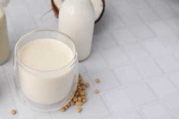 Different types of vegan milk and ingredients on white tiled table, closeup. Space for text