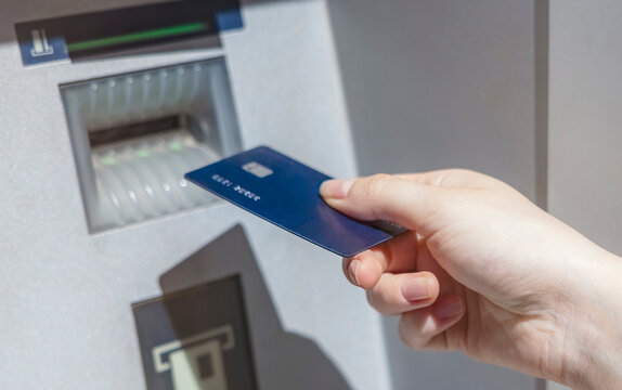 A women&rsquo;s hand inserts a blue credit card into an ATM card reader. Women&rsquo;s hand with manicure and a banking card.
