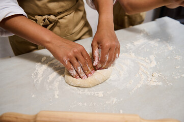 Close-up of hands kneading dough on a floured surface in kitchen