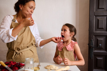 Mother and daughter baking together in kitchen, tasting ingredients and enjoying quality family time