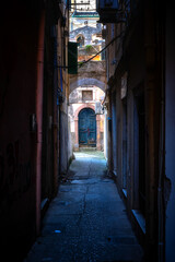 Sehr enge und dunkle Gasse in Korfu Stadt mit Blick auf eine Tür mit Rundbogen