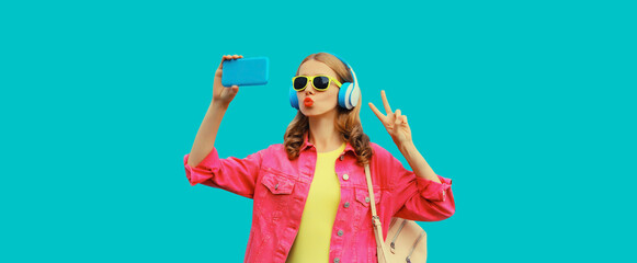 Stylish young woman taking selfie with smartphone listening to music with headphones using phone