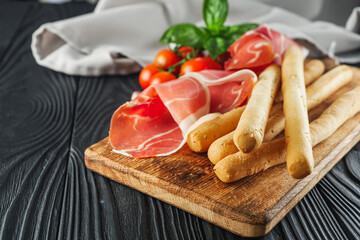 crispy grisini with prosciutto on a black wooden rustic background