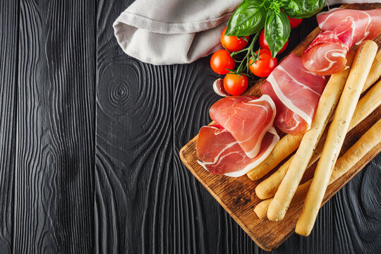crispy grisini with prosciutto on a black wooden rustic background