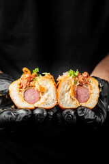 Close-up of a hand-held sausage sandwich with toppings against a dark background