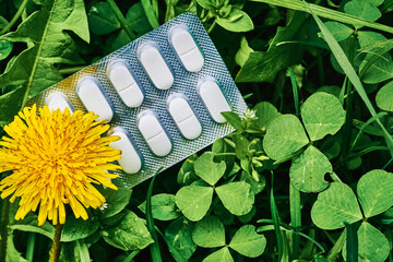White pills in plastic blister on green grass and dandelions on meadow