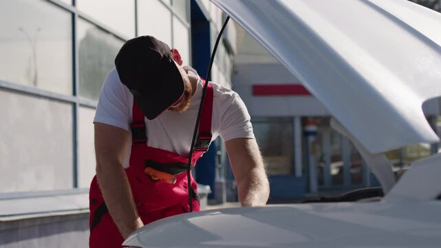 Technician dressed in uniform and chipotle repairs under the hood using a quality mechanical repair wrench. Experts in car repairs. Electrician of a car service makes repairs in car maintenance