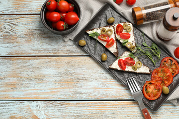 Delicious ricotta bruschettas with fresh tomatoes, olives and greens on wooden table, flat lay. Space for text