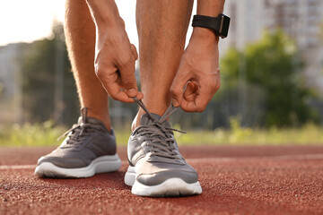Man tying shoelace of grey sneaker at stadium, closeup