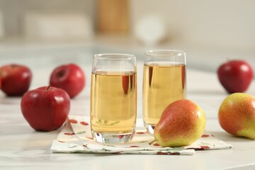 Glasses of fresh juice, pears and apples on white marble table in kitchen