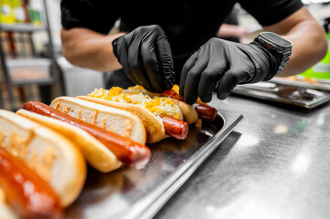Hands in black gloves preparing hot dogs with condiments. This captures the fast food preparation process