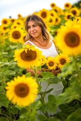 Junge Frau mit Hut steht in einem Sonnenblumenfeld und lächelt  bei schönem Wetter im Sonnenlicht.