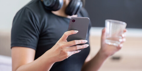 Woman in Activewear Holding Smartphone and Water Glass After Workout, Ready for Hydration and Fitness Tracking