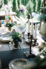 Beautiful summer dinner table setting outdoors, with vintage plates, candles, wine glasses and jasmine and forget me not flowers on the wooden table 