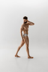 Side view photo of athletic young man in white underwear posing holding hand on neck against white studio background. Muscular build. Concept of male health, body care, natural beauty people, fitness.