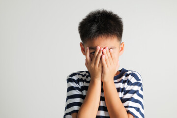 Asian portrait young kid boy in depressed bad mood covering face with hands and peering out with one eye between fingers studio shot isolated on white background, primary child surprised and shocked