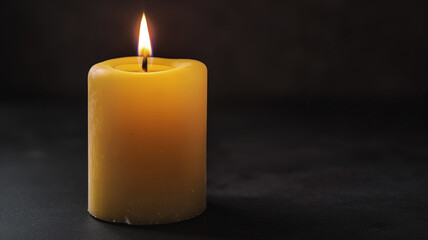 Lit yellow candle against a dark background creating a warm and peaceful atmosphere. The soft glow of the flame adds a sense of calm and tranquility