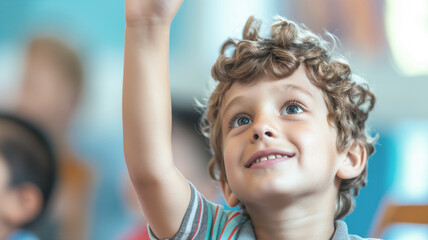 Curly-haired boy raising his hand in a classroom with a smile on his face. The background shows other children, indicating an engaging and interactive learning environment