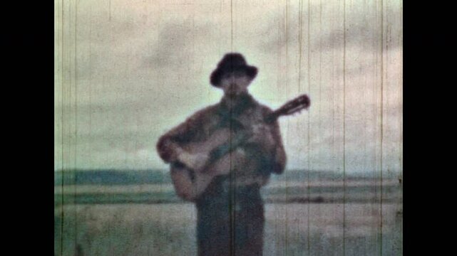 Musician portrait, walk through field nature, sing songs. Music artist performance on natural meadow background. Romantic man play guitar in summer outdoors. Vintage color film. Retro 1960s archive