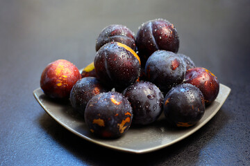 Fresh ripe red purple plums covered with water drops on a plate on dark background