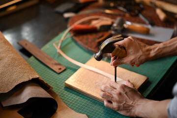 Male artisan holding a tool and a hammer to puncture or shape the leather on a workbench