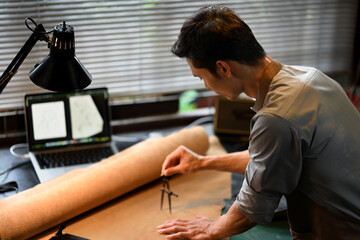 Close up of an artisan hands meticulously measuring a piece of leather using a pair of dividers in workshop