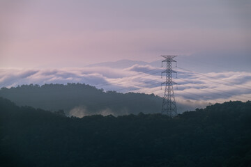 Obraz premium A high voltage tower and a sea of raging, tumbling clouds on a summer morning. View of the mountains surrounding Emerald Reservoir. Xindian District, Taiwan.