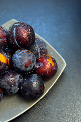 Fresh ripe purple plums covered with water drops in a plate on dark background