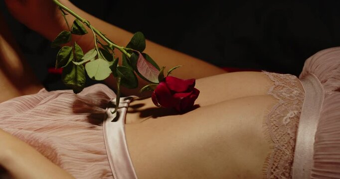 Close up of a beautiful red rose seductively caressing the belly and lower body of an attractive woman dressed in lingerie