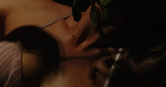 An attractive woman dressed in sexy lingerie enticingly plays with a rose and caresses her face with the red flower