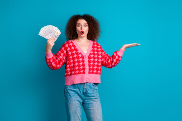 Photo of cheerful impressed lady dressed red cardigan holding money fan showing arm empty space isolated blue color background