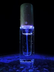 The perfume is illuminated with blue neon light. Perfume water in close-up on a black background. Background, place for text. Men's perfume. Splashes of water. Perfume bottle.