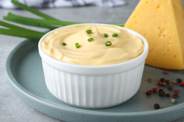 Tasty cheese sauce with green onion and peppercorns on light grey table, closeup