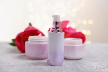 Set of different cosmetic products and peony flower on gray table against light background with blurred lights, closeup