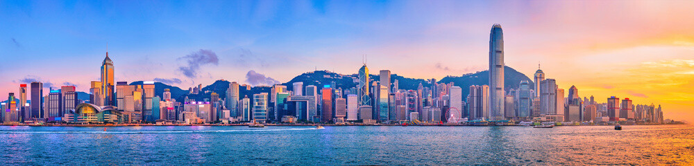 Panorama of Hong Kong skyline cityscape downtown skyscrapers over Victoria Harbour in the evening with junk tourist ferry boat on sunset with dramatic sky. Hong Kong, China